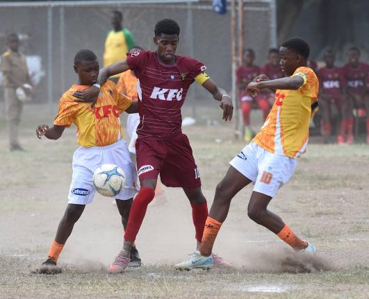Garfield Massop (centre) of Denham Town High attempts to force his way between Joseph Ward (left) and Kwasi Clarke of Donald Quarrie High during their Manning Cup football match at Tivoli High School yesterday.