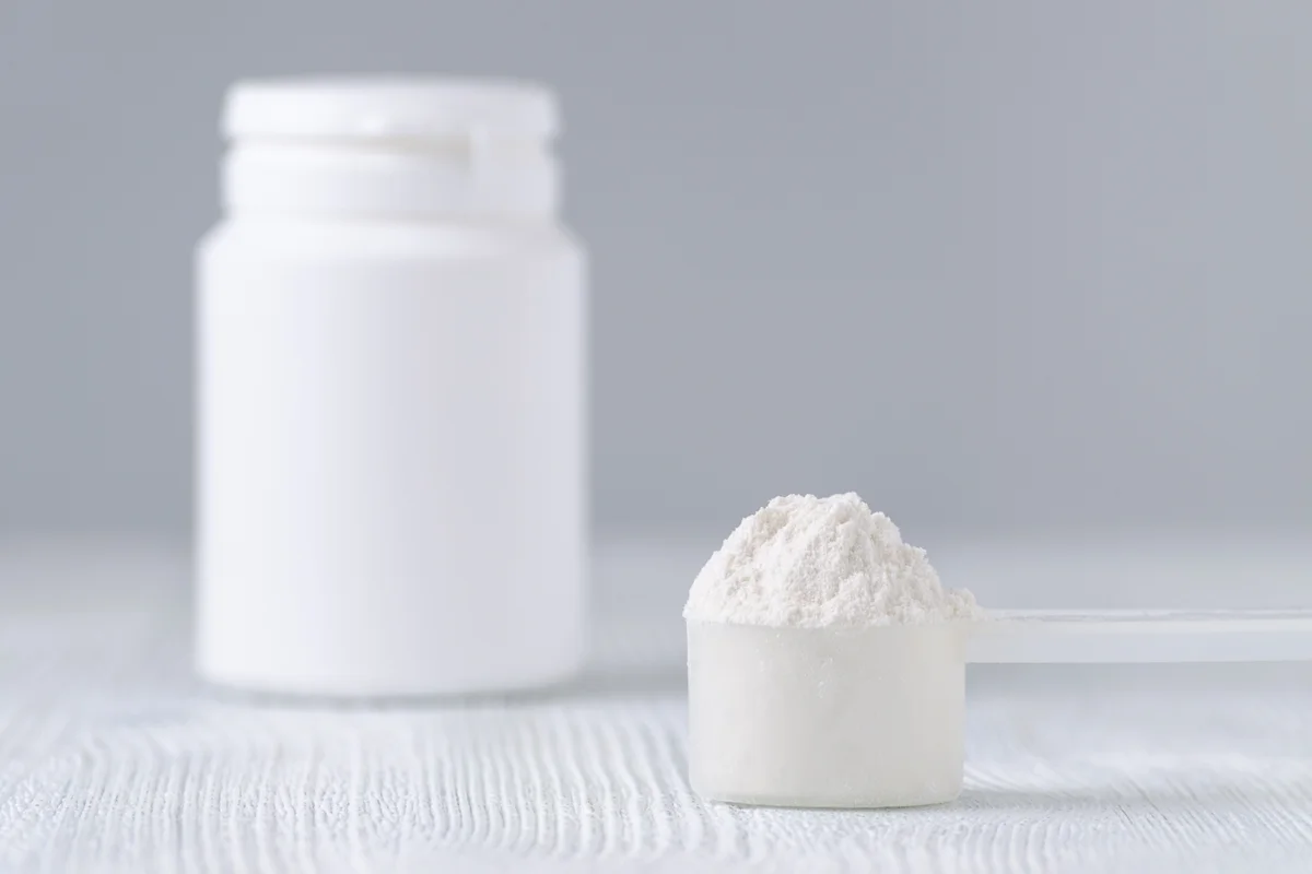 Imagem mostra um scoop com pó branco e ao fundo um pote também branco. Conceito de whey protein, creatina ou suplemento. Metrópoles