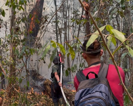 A man sprays water into smoke-filled forest as another stands behind him