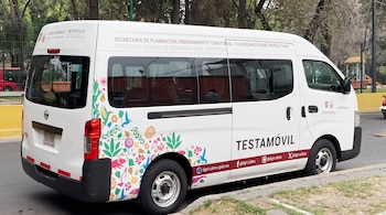 Una camioneta blanca decorada con ilustraciones florales y la palabra Testamóvil, estacionada junto a una acera.