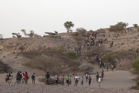 People walk along a path leading up a hill through scrubland